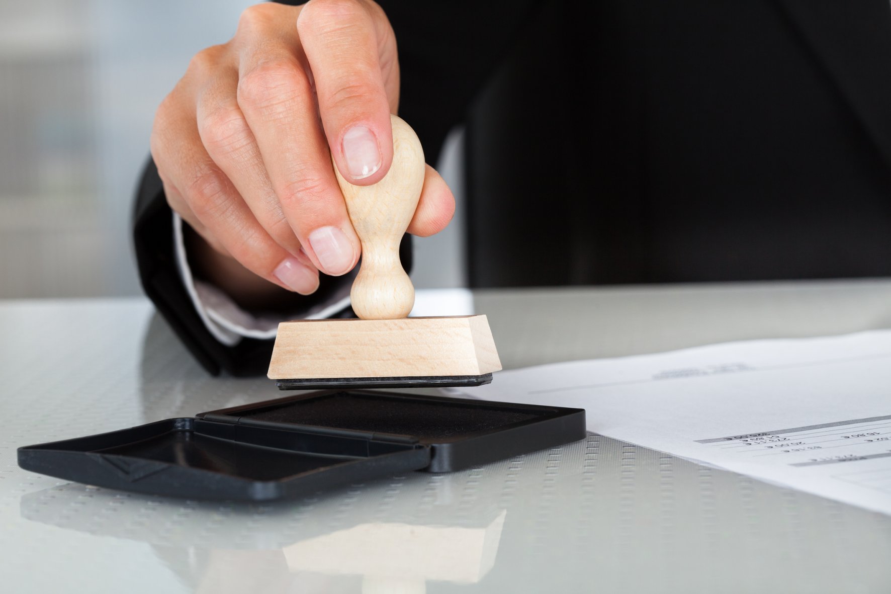 Close-up Of Business Man Hand Pressing Rubber Stamp On Document Close-up Of Business Man Hand Pressing Rubber Stamp On Document