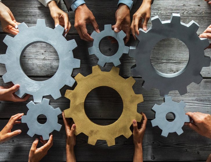 Group of business people joining together silver and golden colored gears on table at workplace top view